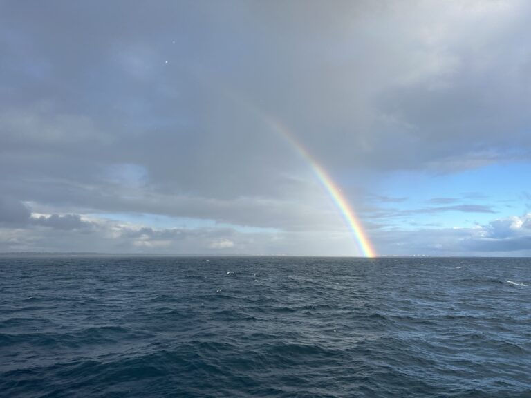 Offenes Meer unter Wolken mit Regenbogen am Horizont