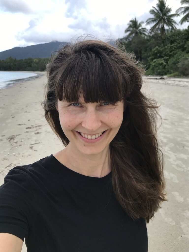 Shireen lacht an einem Strand mit Palmen in Australien